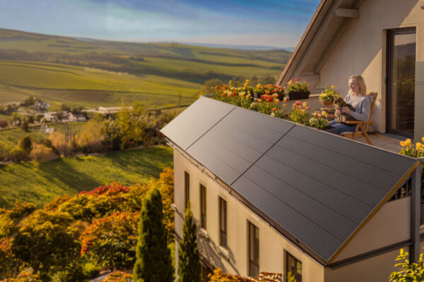 Eine Frau sitzt auf einer Terrasse neben einer Balkonsolar-Anlage, mit Blumen und weiter Hügellandschaft im warmen Licht.